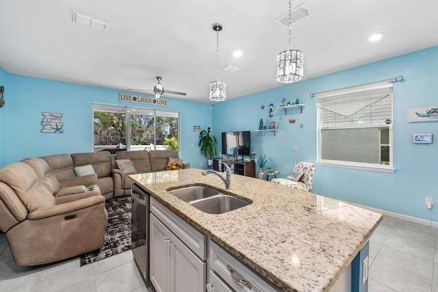 kitchen featuring ceiling fan, sink, light stone countertops, decorative light fixtures, and a kitchen island with sink