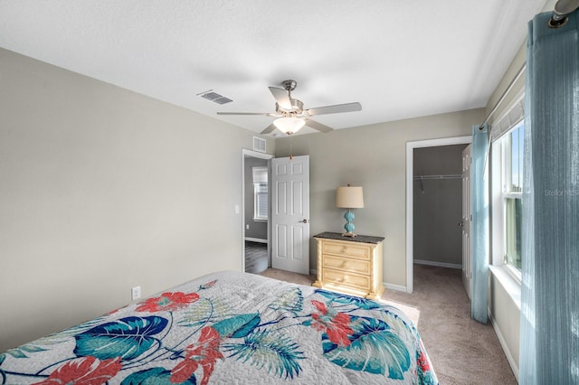 carpeted bedroom featuring a walk in closet, a closet, and ceiling fan