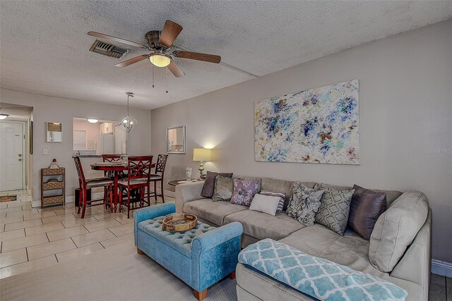 tiled living room with a textured ceiling and ceiling fan with notable chandelier