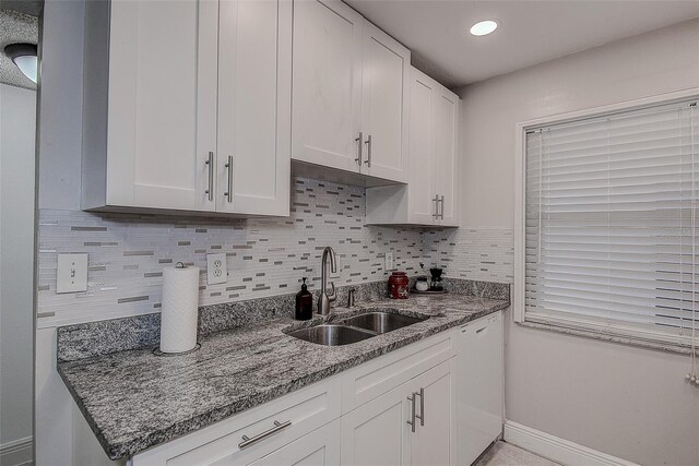 kitchen with backsplash, sink, stone counters, dishwasher, and white cabinets