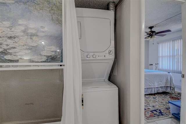 laundry area with stacked washer and dryer, tile patterned flooring, a textured ceiling, and ceiling fan