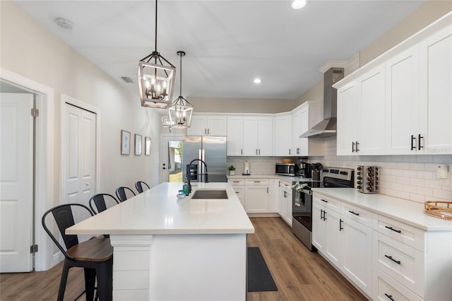 kitchen featuring a kitchen breakfast bar, wall chimney exhaust hood, stainless steel appliances, sink, and an island with sink