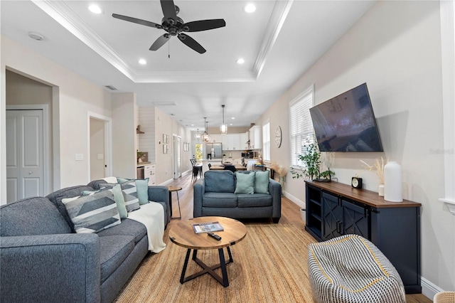 living room featuring ceiling fan, ornamental molding, a tray ceiling, and light hardwood / wood-style floors