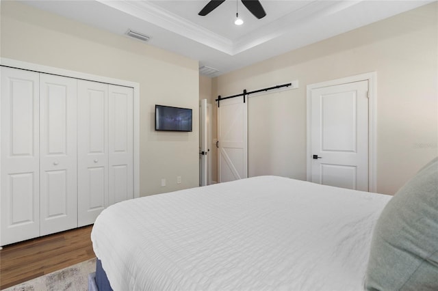 bedroom featuring hardwood / wood-style flooring, ceiling fan, a barn door, ornamental molding, and a tray ceiling