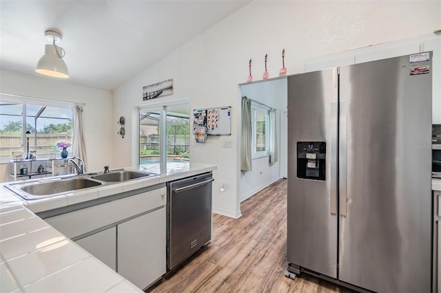 kitchen featuring light hardwood / wood-style flooring, vaulted ceiling, white cabinetry, appliances with stainless steel finishes, and sink