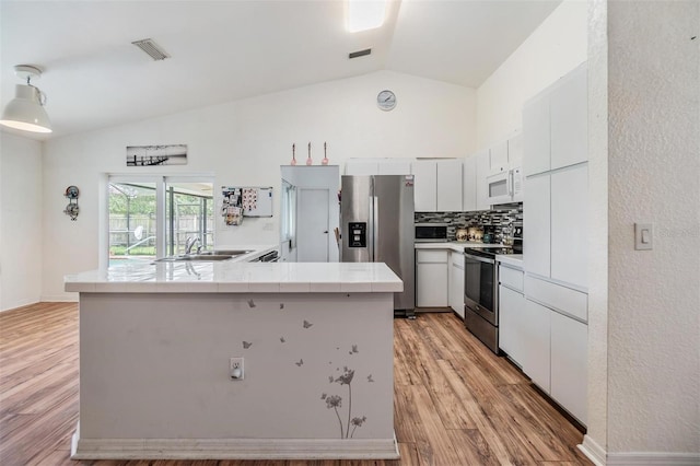 kitchen featuring light hardwood / wood-style flooring, white cabinets, vaulted ceiling, appliances with stainless steel finishes, and sink