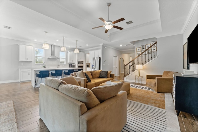 living room with a raised ceiling, light wood-type flooring, ceiling fan, and ornamental molding