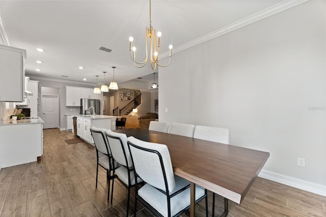 dining room with a notable chandelier, crown molding, sink, and wood-type flooring