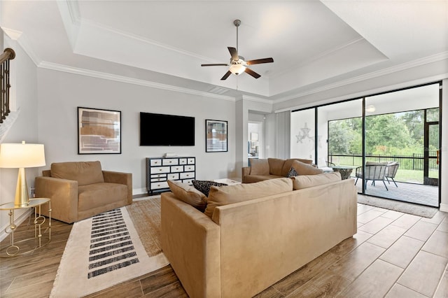 living room featuring light wood-type flooring, crown molding, ceiling fan, and a raised ceiling