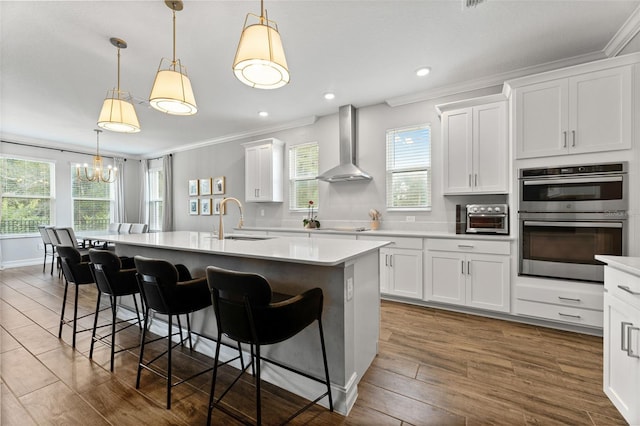 kitchen with a kitchen island with sink, sink, white cabinets, wall chimney exhaust hood, and pendant lighting