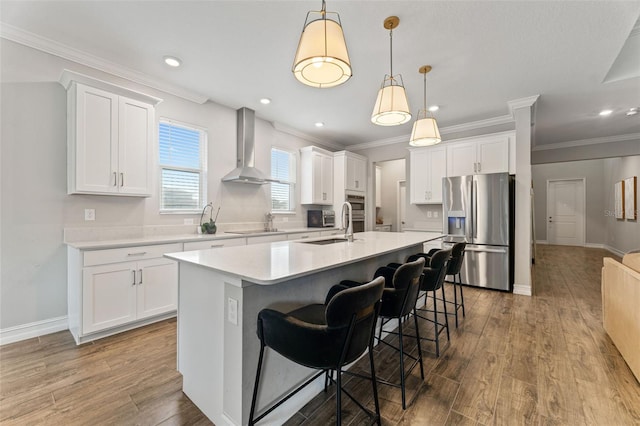 kitchen featuring a center island with sink, decorative light fixtures, stainless steel refrigerator with ice dispenser, white cabinets, and wall chimney exhaust hood