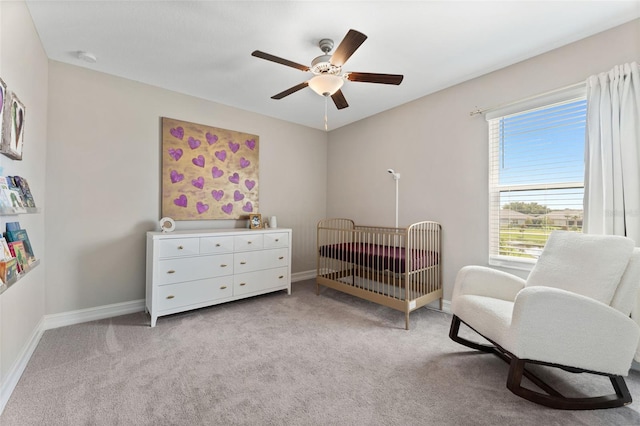 carpeted bedroom with a crib and ceiling fan