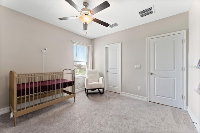 carpeted bedroom featuring a crib and ceiling fan