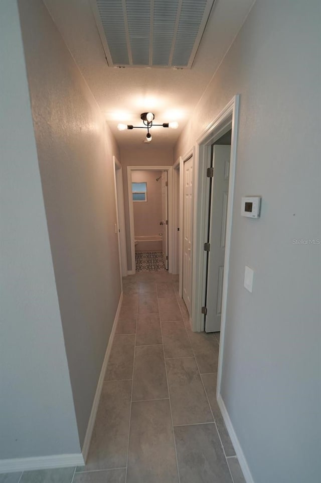 corridor with light tile patterned floors, visible vents, and baseboards