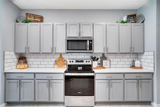 kitchen featuring gray cabinetry, stainless steel appliances, light tile patterned floors, and backsplash