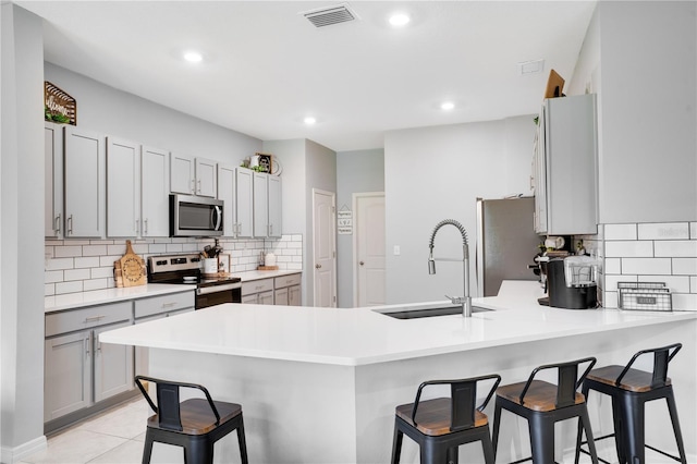 kitchen featuring stainless steel appliances, a breakfast bar, backsplash, light tile patterned flooring, and sink