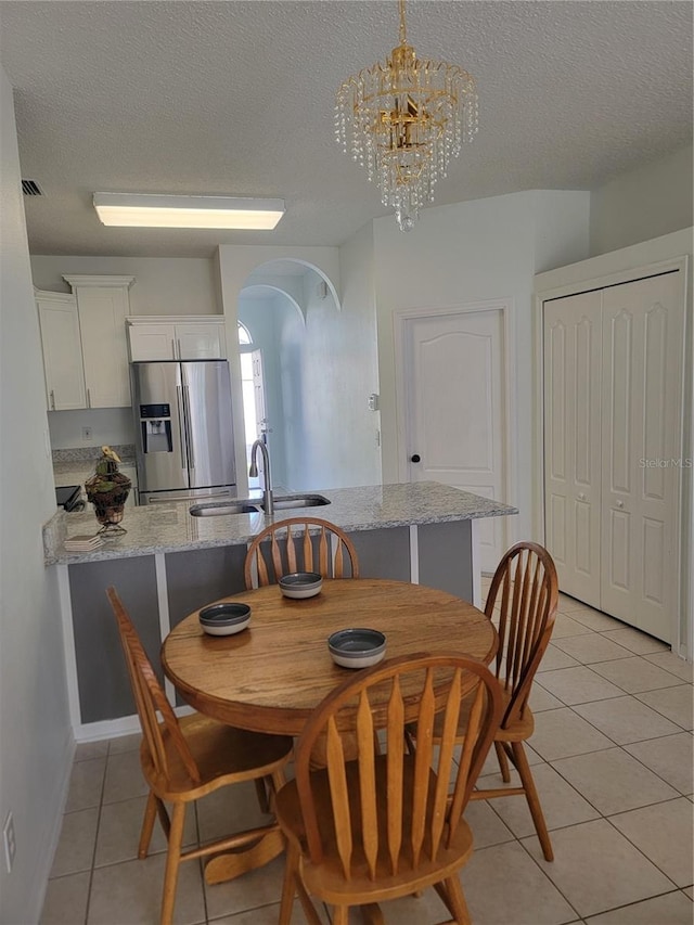 dining area with sink, light tile patterned floors, a textured ceiling, and an inviting chandelier