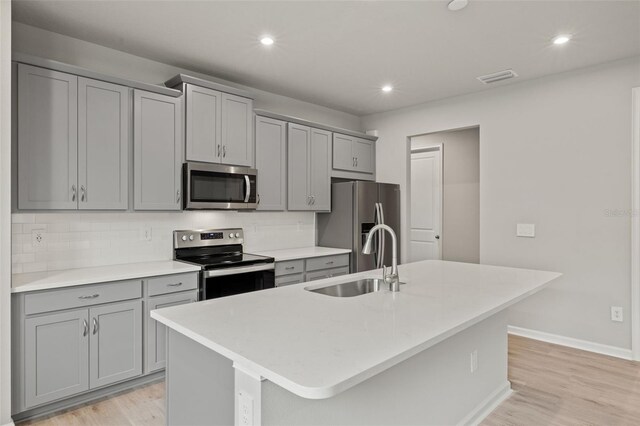 kitchen featuring light hardwood / wood-style flooring, stainless steel appliances, an island with sink, sink, and decorative backsplash