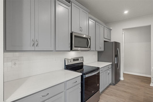 kitchen with stainless steel appliances, gray cabinets, decorative backsplash, and light hardwood / wood-style floors