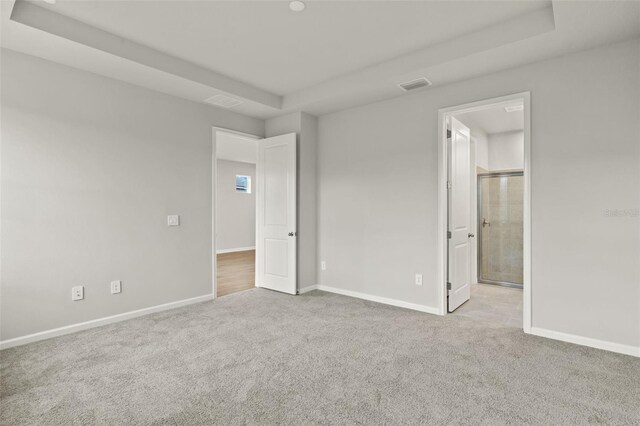 unfurnished bedroom featuring ensuite bath, light carpet, and a tray ceiling