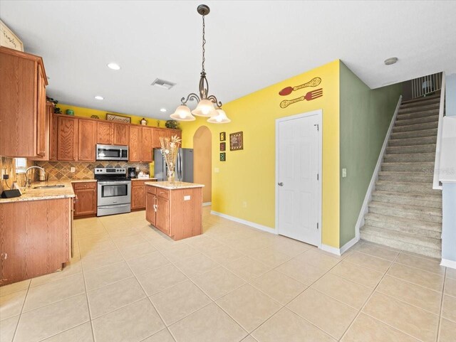 kitchen with appliances with stainless steel finishes, decorative backsplash, sink, pendant lighting, and a kitchen island