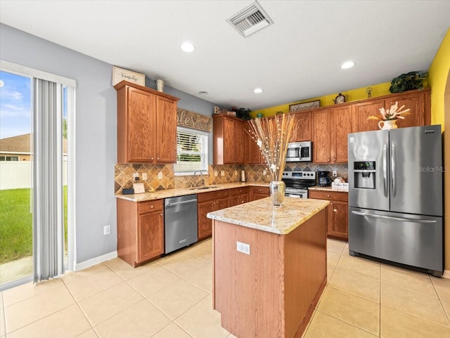 kitchen with a center island, appliances with stainless steel finishes, light stone countertops, tasteful backsplash, and light tile patterned floors