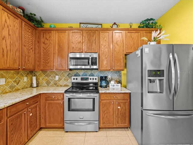 kitchen with appliances with stainless steel finishes, light stone counters, light tile patterned flooring, and tasteful backsplash