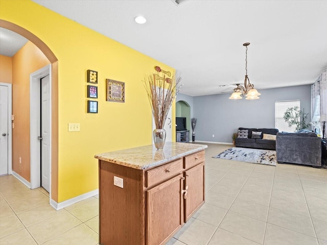 kitchen featuring light tile patterned flooring, light stone countertops, a kitchen island, ceiling fan, and pendant lighting