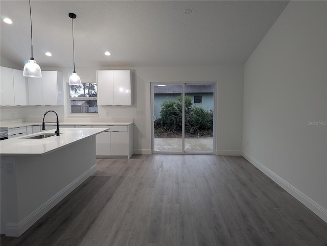 kitchen with sink, hardwood / wood-style flooring, white cabinetry, hanging light fixtures, and a center island with sink