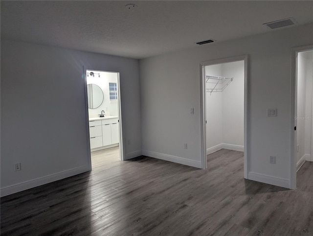 interior space with sink, a walk in closet, dark wood-type flooring, ensuite bath, and a closet