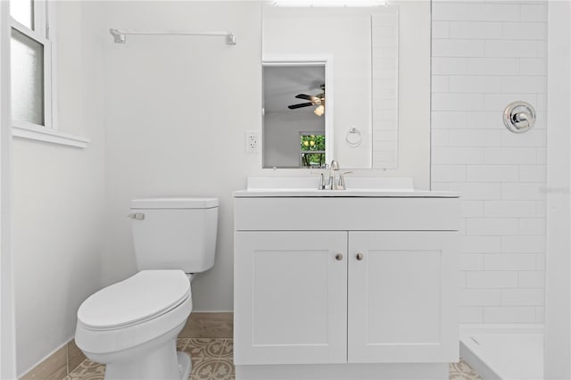 bathroom featuring toilet, ceiling fan, vanity, tiled shower, and baseboards