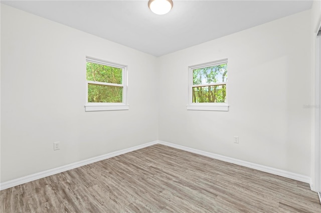 spare room featuring baseboards, light wood-type flooring, and a healthy amount of sunlight