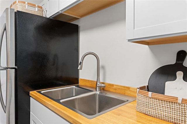 room details featuring butcher block countertops, freestanding refrigerator, white cabinetry, and a sink