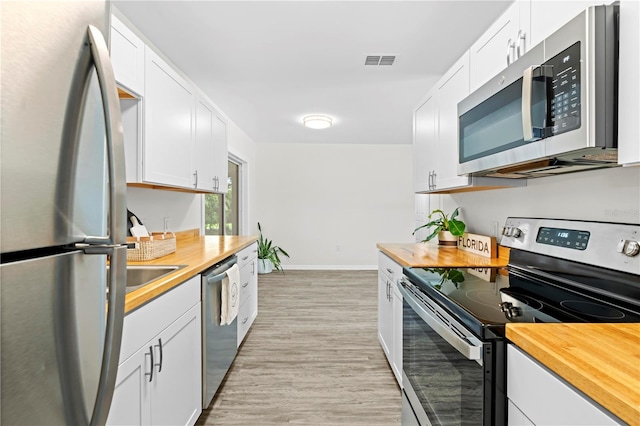 kitchen featuring appliances with stainless steel finishes, light hardwood / wood-style flooring, white cabinets, and wooden counters