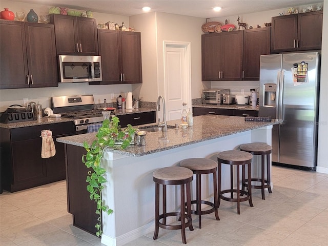 kitchen with light tile patterned floors, sink, stainless steel appliances, and an island with sink