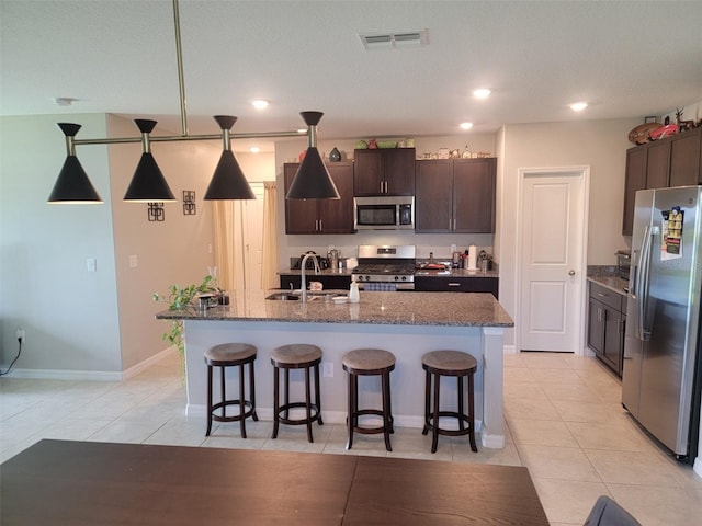 kitchen featuring light tile patterned floors, appliances with stainless steel finishes, a kitchen island with sink, and decorative light fixtures