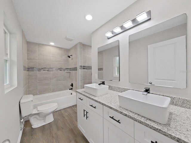 full bathroom with tiled shower / bath, double sink vanity, toilet, and hardwood / wood-style flooring