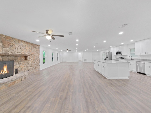 unfurnished living room featuring ceiling fan, light wood-type flooring, sink, and a fireplace