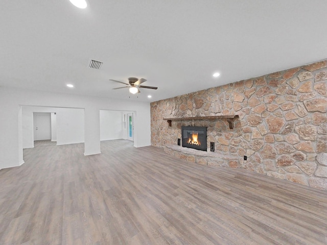 unfurnished living room with ceiling fan, a stone fireplace, and light wood-type flooring