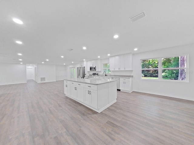 kitchen featuring sink, light wood-type flooring, appliances with stainless steel finishes, an island with sink, and white cabinets