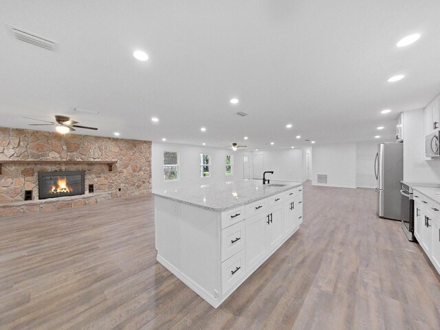 kitchen featuring a stone fireplace, sink, light stone counters, appliances with stainless steel finishes, and white cabinets