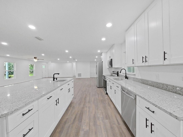 kitchen with sink, appliances with stainless steel finishes, white cabinetry, light stone counters, and wood-type flooring