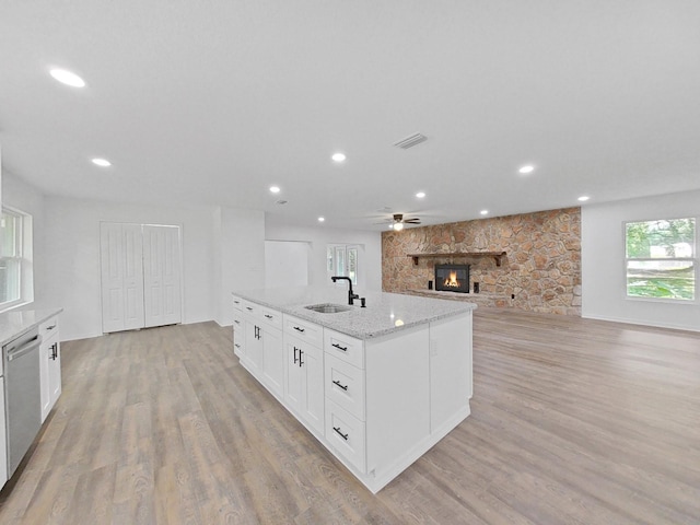 kitchen with a stone fireplace, sink, light stone counters, stainless steel dishwasher, and white cabinets