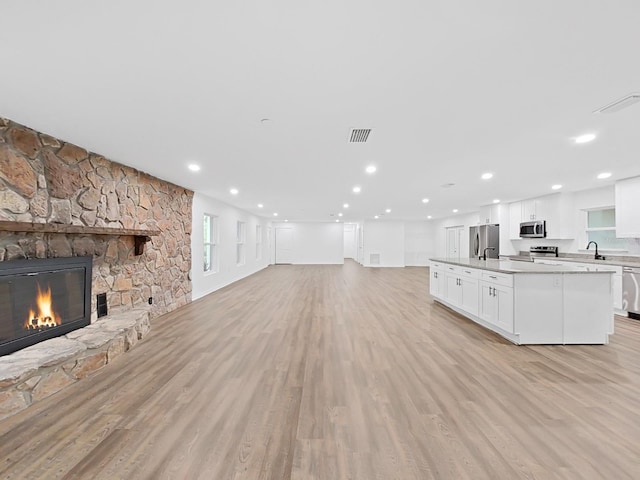 unfurnished living room featuring a stone fireplace, sink, and light hardwood / wood-style floors