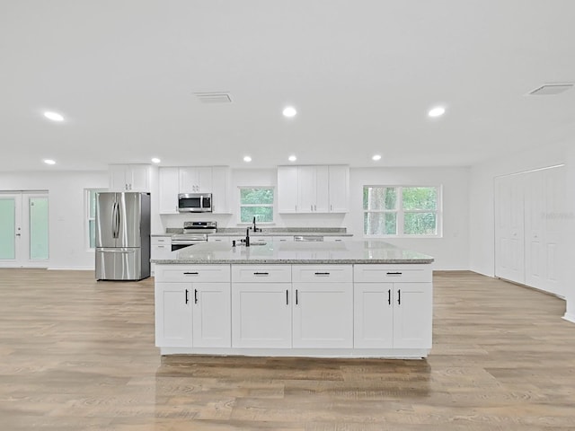 kitchen with stainless steel appliances, white cabinetry, and light stone countertops