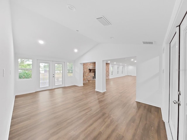 unfurnished living room with lofted ceiling, a fireplace, light hardwood / wood-style flooring, and french doors