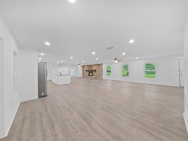 unfurnished living room with ceiling fan, a fireplace, and light wood-type flooring