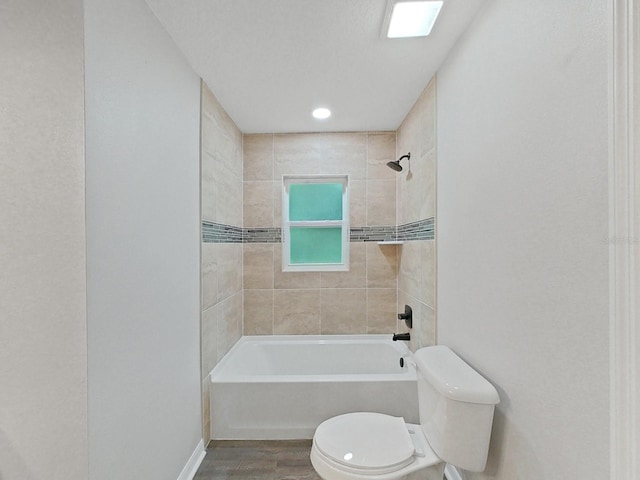 bathroom with hardwood / wood-style flooring, tiled shower / bath, and toilet