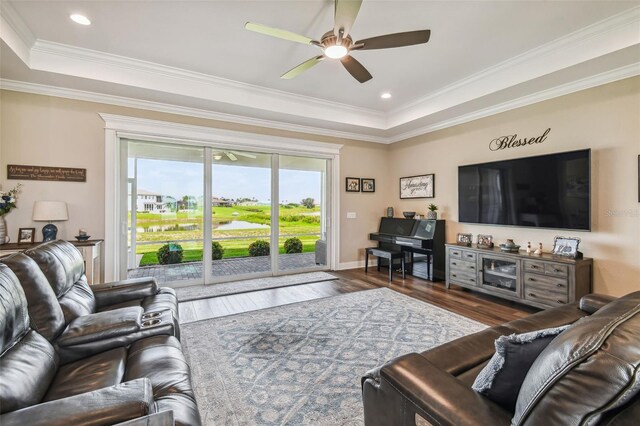 living room with a tray ceiling, ceiling fan, dark hardwood / wood-style flooring, and ornamental molding