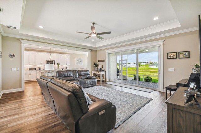 living room featuring ceiling fan, a raised ceiling, light hardwood / wood-style flooring, and ornamental molding